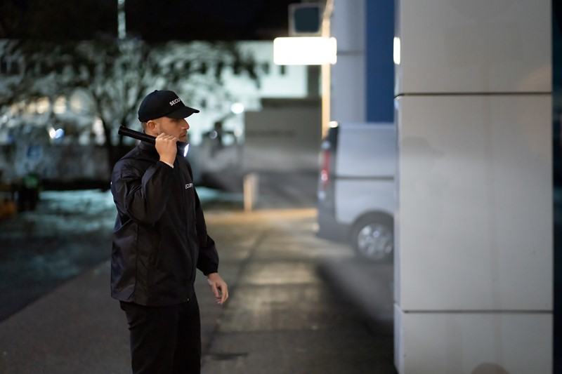 Ein Beamter kontrolliert ein Gebäude mit einer Taschenlampe in seiner Hand. Seine Kopfbedeckung besagt ''Security''.