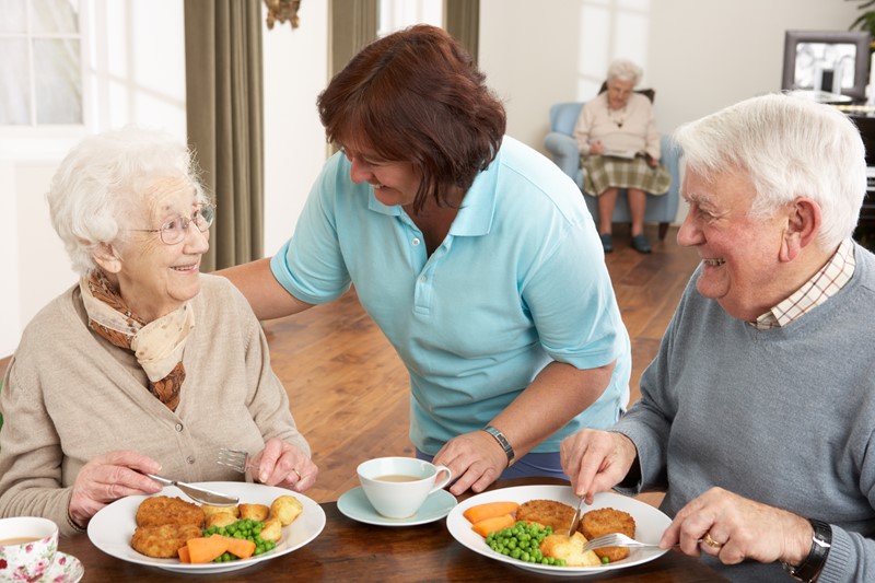 Pflegerin serviert einem älteren Paar ein Gericht.